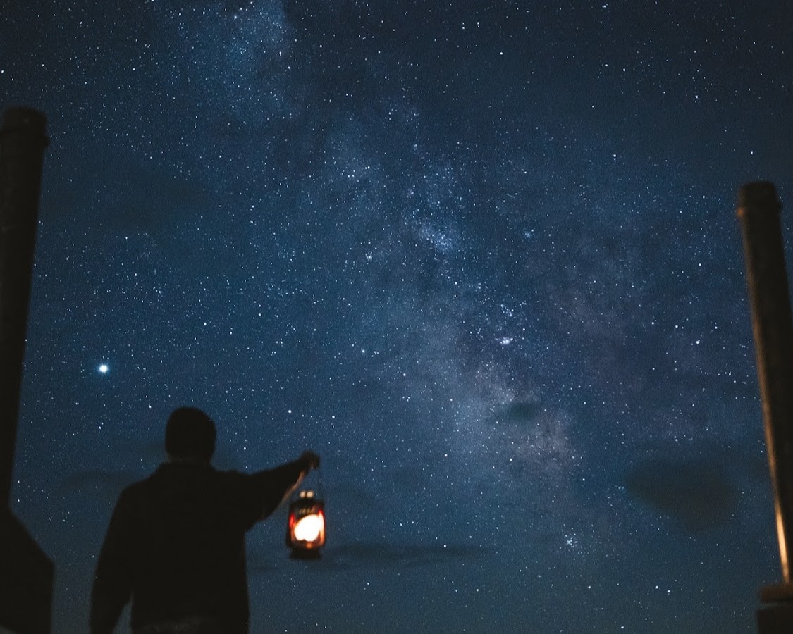 A Staff member holding a lantern below the night sky at Many Point, where the milky way galaxy is visible