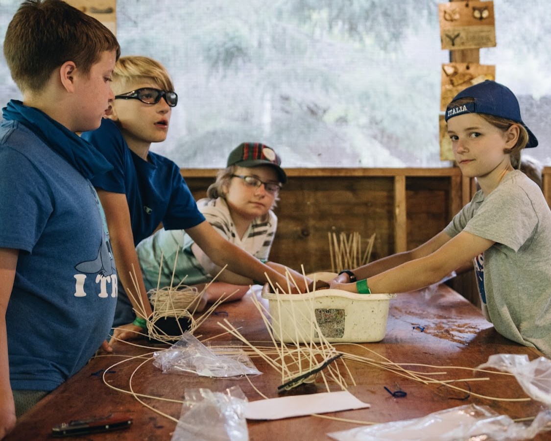 Four Scouts mid-weaving baskets on a table