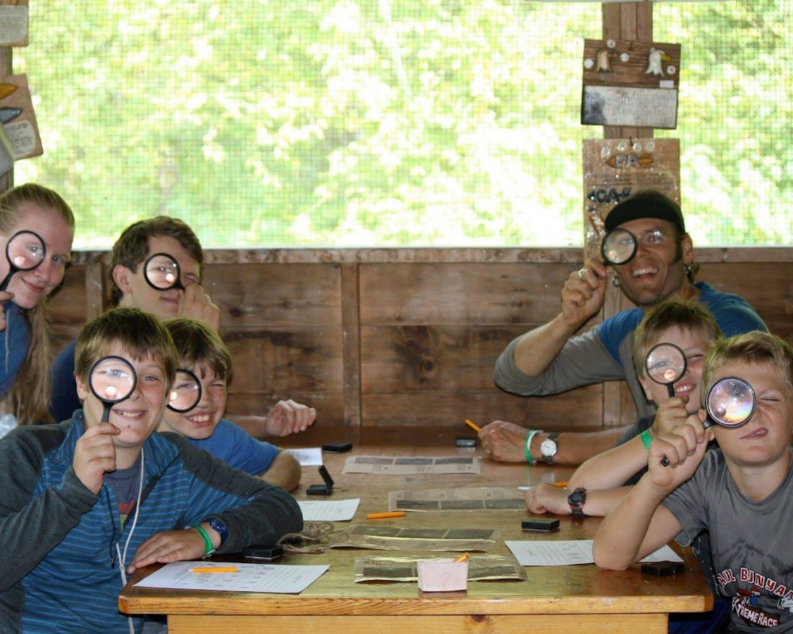 A group of Scouts around a table use magnifying glasses to look at the camera