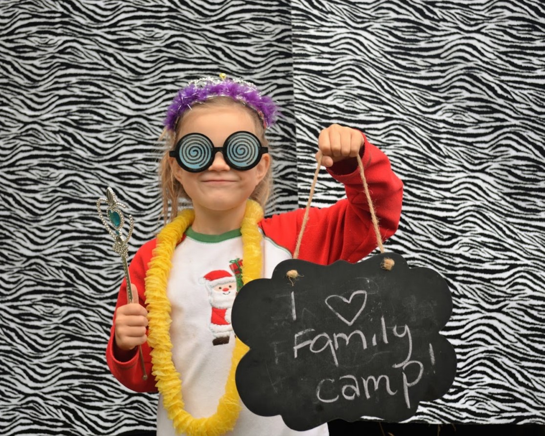 A young girl wearing a lei holding a sign that says 'I heart Family Camp'