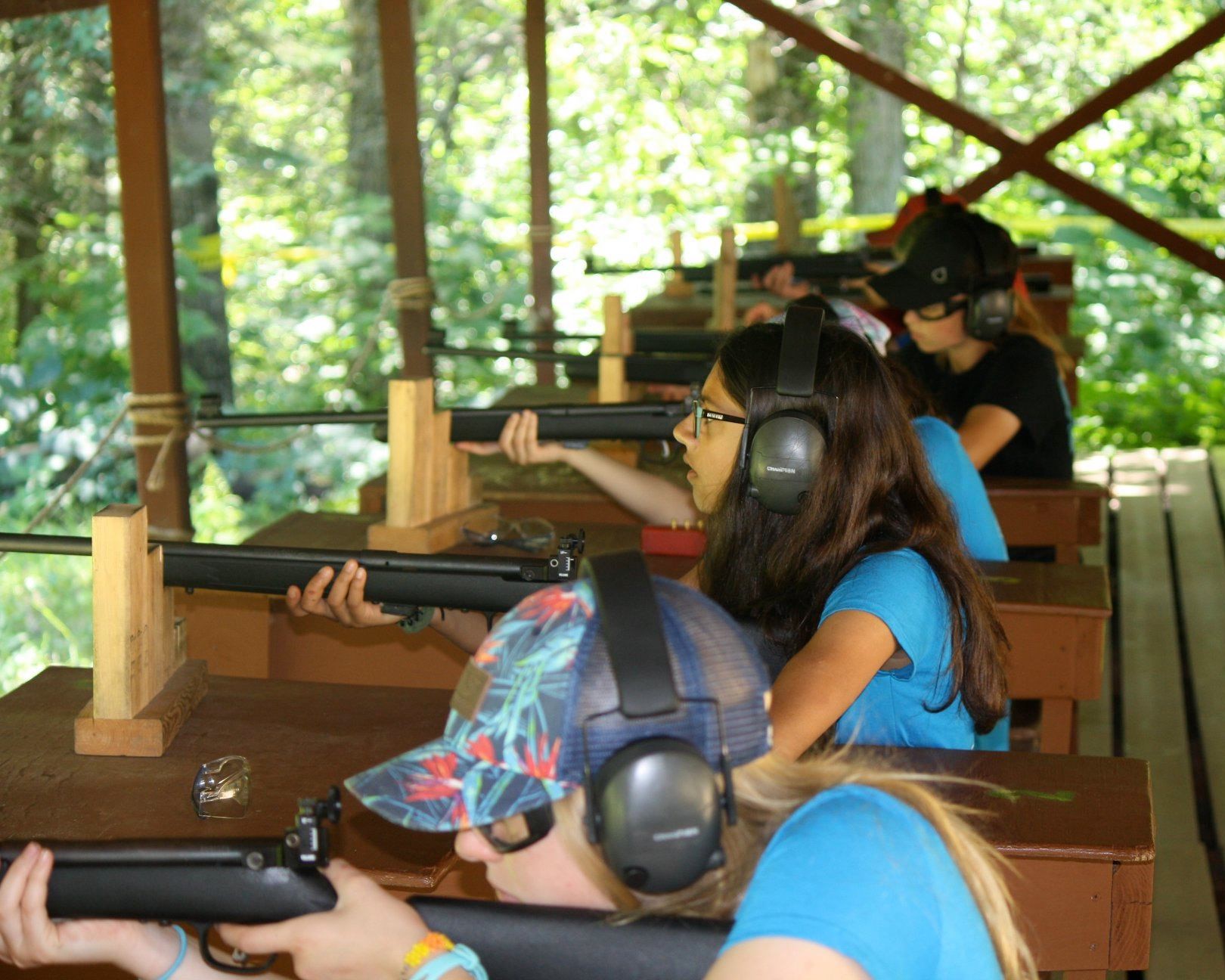 A group of Scouts wearing safety glasses and earmuffs are shooting rifles at the range